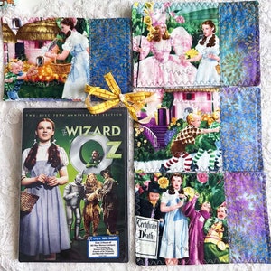May include: A set of four colorful fabric coasters featuring scenes from the Wizard of Oz movie. The coasters are decorated with images of Dorothy, the Wicked Witch of the West, the Scarecrow, the Tin Man, and the Cowardly Lion. The coasters are tied together with a yellow ribbon and a DVD of the Wizard of Oz movie is in the background.