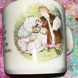 May include: White ceramic mug featuring a whimsical illustration of a child and a hedgehog in vintage clothing. The artwork is in soft pastel colors, with text on the side. The mug has a curved handle.