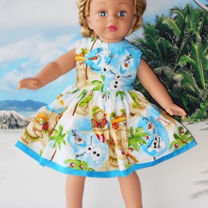 Pode incluir: Um vestido branco com uma borda azul e uma estampa tropical com Olaf de Frozen. O vestido tem palmeiras, bonecos de neve e Olaf usando um colar de flores.