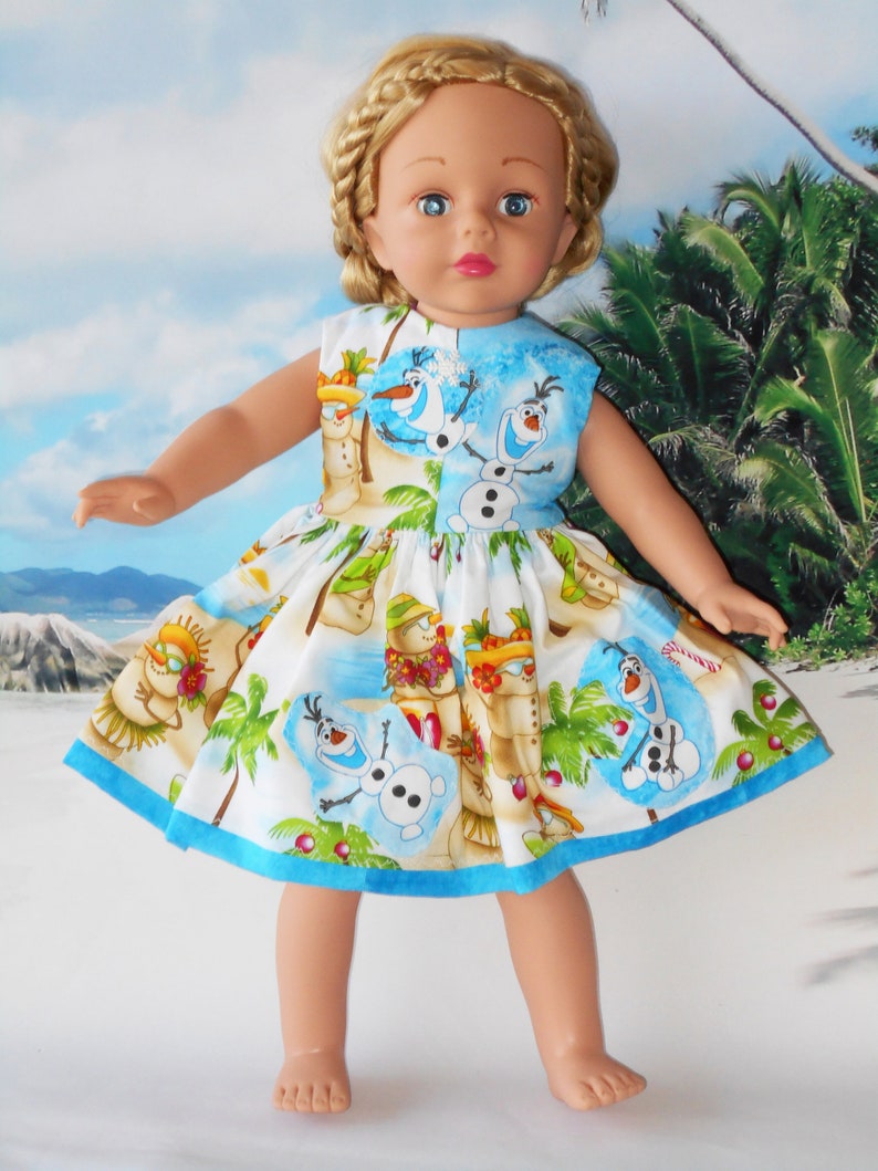 Pode incluir: Um vestido branco com uma borda azul e uma estampa tropical com Olaf de Frozen. O vestido tem palmeiras, bonecos de neve e Olaf usando um colar de flores.