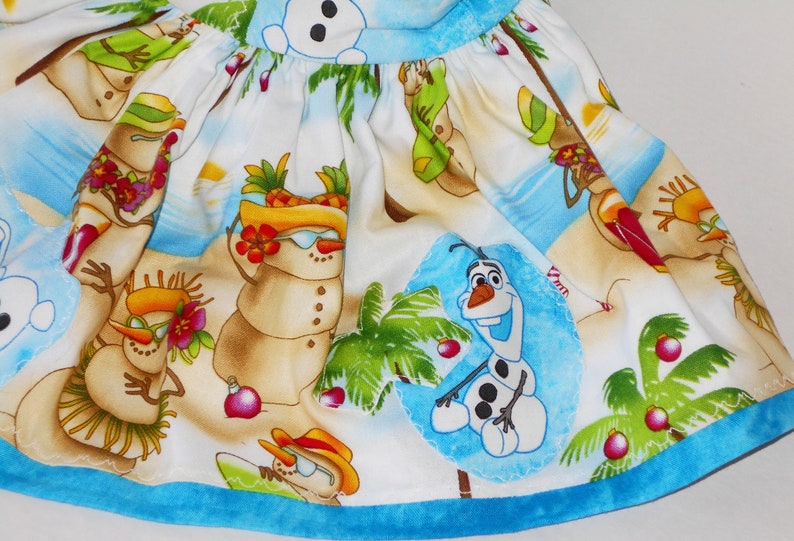 Pode incluir: Um tecido branco com uma bainha azul apresenta uma cena de praia tropical com bonecos de neve usando &oacute;culos de sol e chap&eacute;us, palmeiras e Olaf de Frozen.