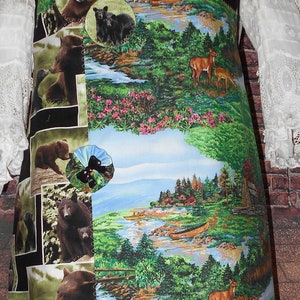 May include: An apron featuring a collage of bear images and a scenic landscape with deer, trees, and a river. The apron has a black border and a decorative bow.