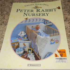 May include: A book cover featuring a nursery decorated with Peter Rabbit themed decor. The cover shows a baby in a crib with a Peter Rabbit themed blanket and a Peter Rabbit themed pillow. The book title is "Create Your Own Peter Rabbit Nursery".