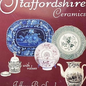 May include: A book titled "Romantic Staffordshire Ceramics" with values by Jeffrey B. Snyder. The cover features a red background with a white swirl design and images of blue and white, green and white, and black and white ceramic plates and a teapot.