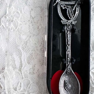 May include: A silver souvenir spoon from Captiva Island, Florida, displayed in a black case with a clear lid. The spoon features a seashell design and the words "Captiva Island". The case has a red velvet insert.