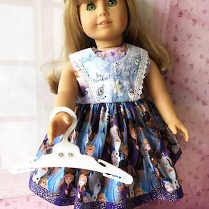 K&ouml;nnte beinhalten: Puppe in einem ma&szlig;geschneiderten Kleid mit Figuren aus dem Animationsfilm. Das Kleid hat ein blaues Oberteil mit dem Text "Ice Breaker!" und einen lila Rock mit Charakterillustrationen. Die Puppe h&auml;lt einen wei&szlig;en Kleiderb&uuml;gel.