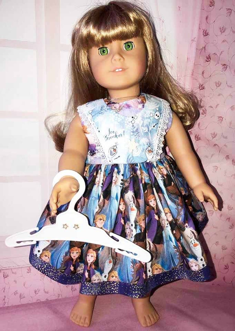 K&ouml;nnte beinhalten: Puppe mit einem blau-violetten Kleid im Frozen-Design. Das Kleid hat eine wei&szlig;e Spitzenborte und den Text "Ice Breaker!". Die Puppe h&auml;lt einen wei&szlig;en Kleiderb&uuml;gel mit sternf&ouml;rmigen Aussparungen.
