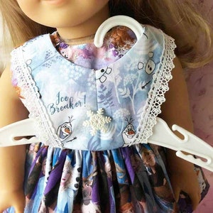K&ouml;nnte beinhalten: Hellblaues Puppenkleid mit wei&szlig;er Spitzenborte und Schneeflockenverzierung. Das Kleid zeigt einen Aufdruck von Figuren und den Text "Ice Breaker!". Es h&auml;ngt an einem wei&szlig;en Kleiderb&uuml;gel.