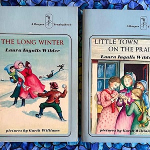 May include: Two vintage children's books, "The Long Winter" and "Little Town on the Prairie" by Laura Ingalls Wilder. The covers feature illustrations of children in winter and prairie scenes. Both books are Harper Trophy Books.