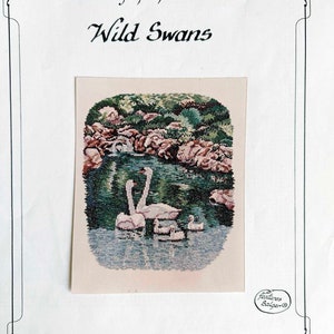 May include: A cross-stitch chart titled "Wild Swans" from the "Across America Series." The image depicts a family of swans on a lake, surrounded by greenery. The chart is from Art Ventures, designed by Jean Lanning.