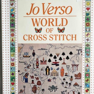 May include: A book titled "Jo Verso World of Cross Stitch" with a colorful cross-stitch design of a world map featuring various cultural symbols and animals.