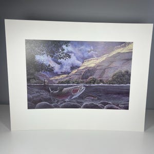 Peut inclure: Une estampe encadrée d'une scène de rivière avec une grande truite sautant hors de l'eau. L'œuvre représente un pêcheur, une chaîne de montagnes et un ciel nuageux. La truite a des marques rouges et argentées. L'estampe est montée sur un passe-partout blanc.