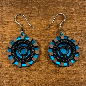 May include: A pair of blue and brown earrings with a circular design. The earrings are shaped like the Arc Reactor from the Iron Man movies.