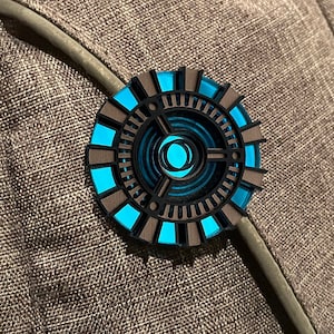 May include: A circular, blue and black, laser-cut, wooden pin with a geometric design.