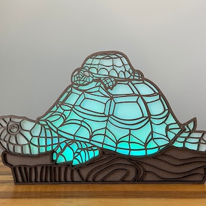 May include: A wooden turtle lamp with a smaller turtle on top. The lamp is lit with a blue and green light.