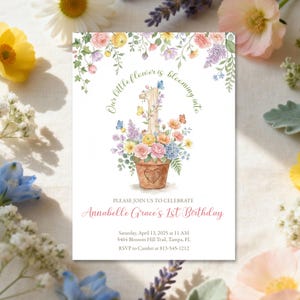 Könnte beinhalten: Eine Einladung zum ersten Geburtstag mit floralem Thema. Das Design zeigt eine Aquarellillustration eines Blumentopfs voller bunter Blumen und Schmetterlinge, mit der Zahl "1" in der Mitte. Der Text lautet "Our little flower is blooming into" und lädt zur Feier von Annabelle Graces erstem Geburtstag ein.
