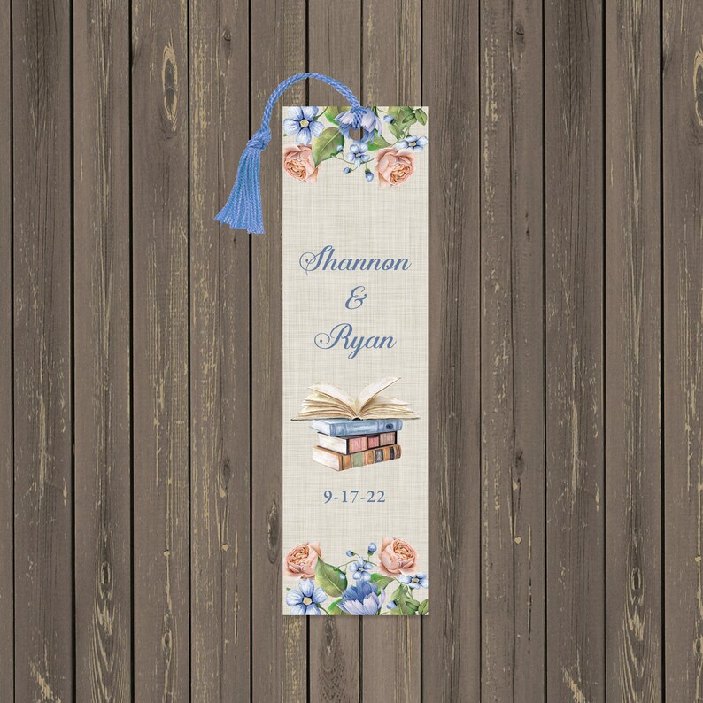 May include: A beige bookmark with a floral design and a stack of books. The bookmark has the names "Shannon & Ryan" and the date "9-17-22" printed on it.