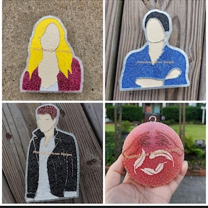 May include: Four glitter resin ornaments. One is a blonde woman with a pink jacket. Another is a man in a blue shirt with arms crossed. The third is a man in a black jacket. The last is a pink ornament with a hand design. All have "Moonstone Manor Designs" text.