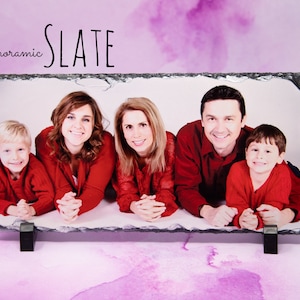 May include: A family of five, two adults and three children, are pictured in a photo printed on a slate plaque. The family is wearing red shirts and are lying on their stomachs with their hands clasped in front of them. The plaque is labeled "panoramic SLATE" in black text.