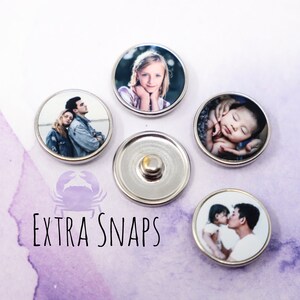 May include: Five round silver-colored snap buttons with different photos printed on them. The photos include a couple, a baby, a young girl, and a father and daughter. The text "EXTRA SNAPS" is printed below the buttons.