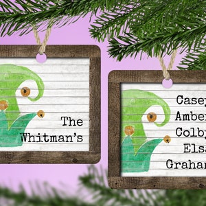 May include: Two wooden Christmas decorations with a green and orange watercolour design. One decoration says "The Whitman's" and the other decoration says "Casey, Amber, Colby, Elsa, Graham".