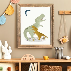 May include: A framed print of a green dinosaur with a smaller yellow dinosaur in its arms. The print has a white background and a crescent moon in the top left corner. The frame is brown wood.