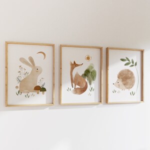 May include: Three framed watercolor illustrations of woodland animals. The first frame features a brown rabbit with a crescent moon above it. The second frame features a red fox with a sun above it. The third frame features a brown hedgehog with a green leaf above it.
