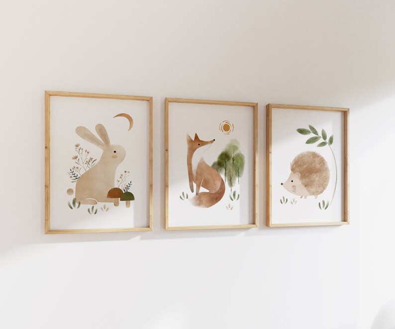May include: Three framed watercolor illustrations of woodland animals. The first frame features a brown rabbit with a crescent moon above it. The second frame features a red fox with a sun above it. The third frame features a brown hedgehog with a green leaf above it.