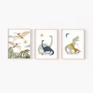 May include: Three framed art prints featuring watercolor illustrations of dinosaurs. The first print shows flying pterodactyls over a landscape. The second print depicts two dinosaurs with a sun. The third print shows a T-Rex with a baby dinosaur.