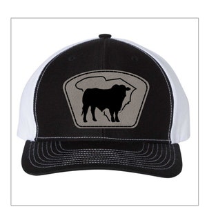 May include: A black and white trucker hat with a gray patch featuring a silhouette of a cow. The hat has a black brim and a white mesh back.