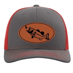 May include: A gray and red trucker hat with a brown leather patch featuring a silhouette of a bass fish jumping out of the water with a dragonfly in its mouth.