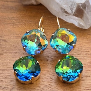 May include: A pair of drop earrings featuring two square-cut, faceted crystals each. The top crystals display iridescent blue and green hues, while the bottom crystals show a vibrant gradient of emerald green transitioning into deep royal blue.