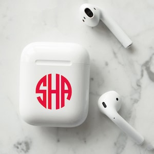 May include: White wireless charging case with a red monogram "SHA" on the front. The case is next to two white wireless earbuds.