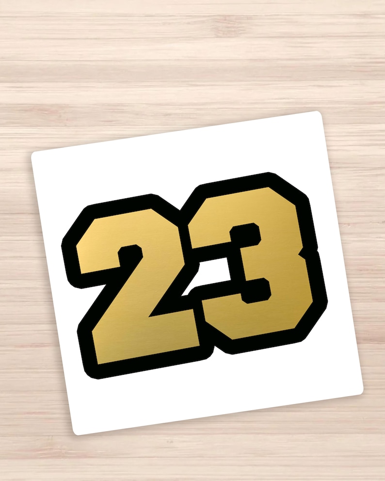 May include: Gold number 23 with a black outline. The number is in a bold, blocky font.