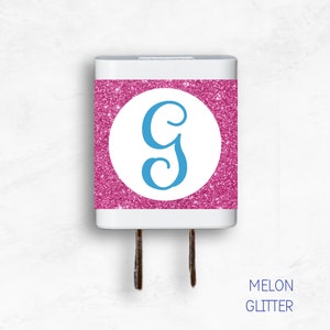 May include: A white phone charger with a pink glitter sticker featuring a blue letter G. The sticker says "MELON GLITTER" at the bottom.