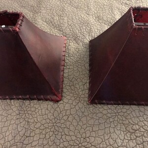 May include: Two burgundy leather lampshades with a stitched edge.