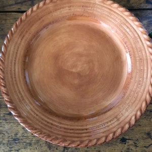 Puede incluir: Un plato de cerámica de color terracota con un diseño de cuerda alrededor del borde. El plato tiene un acabado ligeramente esmaltado y es perfecto para servir comida.