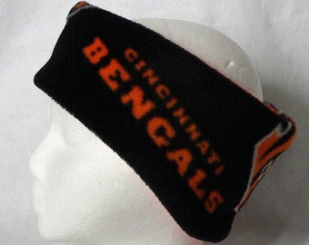 May include: Black fleece headband with the words "CINCINNATI BENGALS" in orange lettering. The headband is displayed on a white mannequin head. The team logo is visible on the right side of the headband.