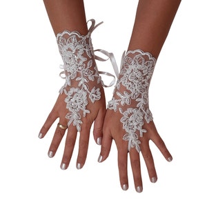 May include: A pair of white lace fingerless gloves with floral designs. The gloves have a ribbon tie at the wrist.