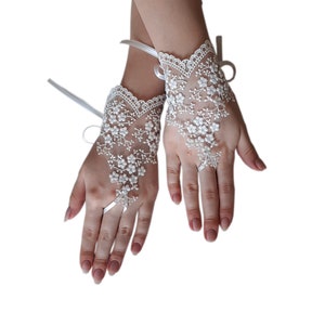 May include: A pair of white lace fingerless gloves with floral embroidery. The gloves have a satin ribbon tie at the wrist.