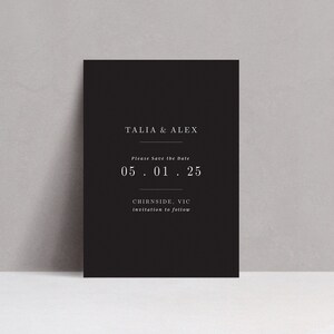 Op de afbeelding: Een zwarte save-the-date kaart met witte tekst. De kaart luidt "TALIA & ALEX" boven de datum "05 . 01 . 25". Onder de datum staat "CHIRNSIDE, VIC invitation to follow". De kaart leunt tegen een lichtgrijze achtergrond.