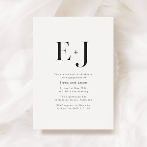 K&ouml;nnte beinhalten: Schlichte Verlobungskarte mit den schwarzen Initialen "E + J" in serifenbetonter Schrift. Der Text gibt die Namen Elena und Jason, Datum, Uhrzeit, Veranstaltungsort und RSVP-Informationen an.