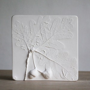 May include: White ceramic wall art with a raised design of two oak leaves and acorns.