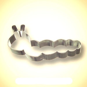 May include: A shiny, silver-colored metal cookie cutter in the shape of a caterpillar. The cutter has a detailed design, with a segmented body and antennae. The cutter is designed for baking and crafting.