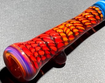 May include: A red, orange and blue glass pipe with a textured, scaly design. The pipe has a rounded mouthpiece and a small, round bowl.