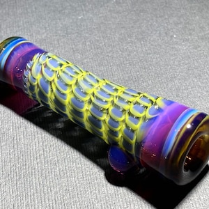May include: A glass smoking pipe with a yellow, blue, and purple swirl design. The pipe has a rounded end and a small, clear glass bead on the side.