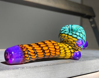 May include: A colourful glass pipe with a blue, yellow and orange swirl design. The pipe has a purple mouthpiece and a small purple accent on the side.
