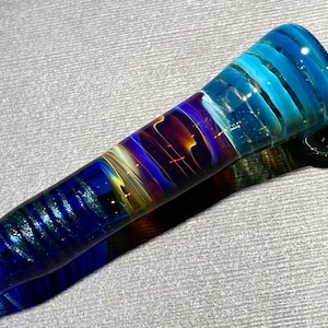 May include: A glass pipe with a blue, purple, and gold swirl design. The pipe is about 6 inches long and has a rounded bowl.