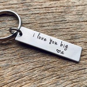 May include: Silver keychain with a rectangular tag that reads "i love you big" with a small heart and the letter "a" engraved on it.