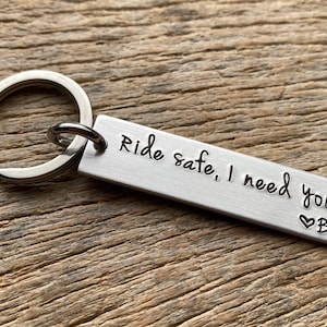 May include: Silver keychain with a rectangular tag that reads "Ride safe, I need you" with a heart and the letter B engraved on the tag.